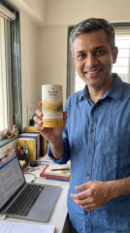 A man beside a window at his work desk, holding the Beyond Better berberine tub